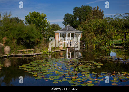 Ampio laghetto in giardino in estate con mattoni summerhouse posti a sedere e si affaccia su acqua e lilles,Giardino,Oxfordshire,Inghilterra Foto Stock