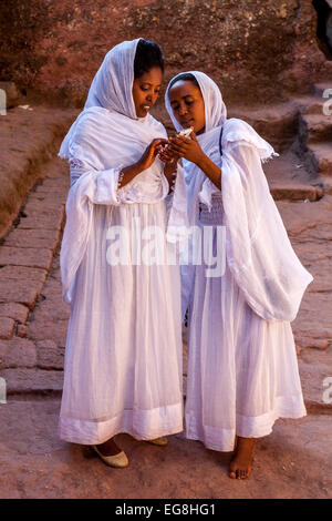 Due pellegrini femmina vestito con i tradizionali abiti bianchi guardare le fotografie su un telefono cellulare, Bete Maryam Chiesa, Lalibela Foto Stock