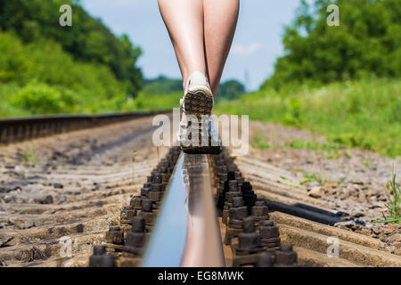 Gambe femmina in sneakers sul binario della linea ferroviaria Foto Stock