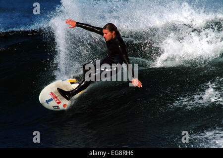 Surfer il taglio di alcune onde pulito in Irlanda invia un pennacchio di spruzzare fuori l'onda come egli accelerare verso il basso la faccia d'onda Foto Stock