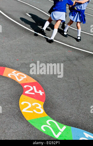 Bambini delle scuole elementari a giocare in un parco giochi scuola a rottura del tempo con numero giochi tracciata sulla superficie dell'asfalto Foto Stock