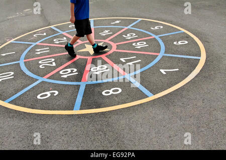 Bambini delle scuole elementari giocando in una scuola parco giochi a tempo di interruzione con numero circolare gioco tracciata sulla superficie dell'asfalto Foto Stock