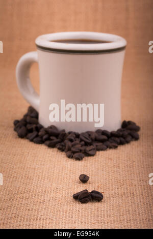 I chicchi di caffè su tela, con una tazza di caffè su sfondo, con molto leggero vignette Foto Stock