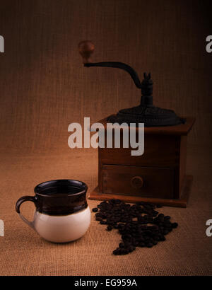 Tazza di caffè con fagioli e un vecchio macinino sullo sfondo, una calda tonalità con immagine vignette Foto Stock