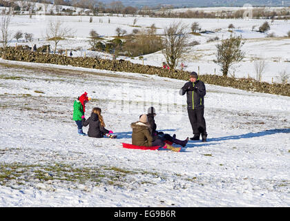 Slittino - uomo si prepara a prendere le foto di famiglia con slitte sul pendio nevoso, Caldbeck fells, Lake District, Cumbria, Inghilterra Foto Stock