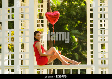 Donna con cuore rosso forma palloncino seduta su una panchina nel parco Foto Stock