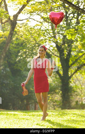 Donna con cuore rosso forma palloncino passeggiate nel parco Foto Stock