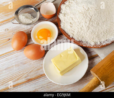 La cottura Ingredienti - uova, farina, zucchero, burro su sfondo di legno Foto Stock