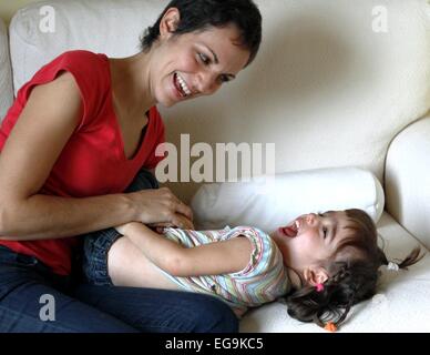 Madre seduti sul divano solletica la figlia Foto Stock