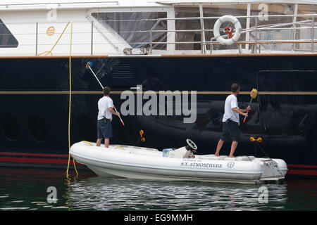 Deckhands in piedi nella gara di un grande yacht di lusso (S.Y. Atmosfera) pulizia della carena. Foto Stock