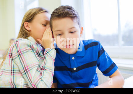 Sorridente schoolgirl whispering a classmate orecchio Foto Stock