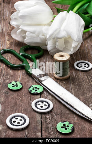 Set di accessori per il cucito da filettature e pulsanti sullo sfondo dei tulipani bianco Foto Stock