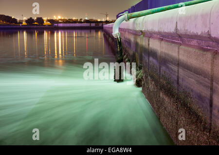 Tubo di fognatura lo scarico di acqua in un fiume di notte. Dubai Creek, EMIRATI ARABI UNITI Foto Stock