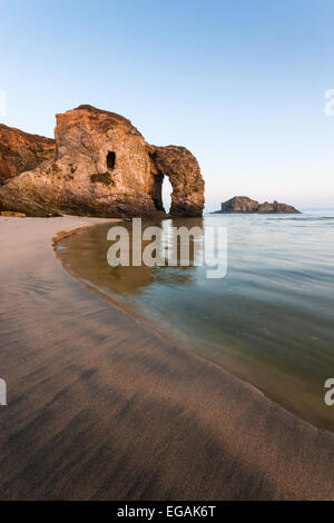 Perranporth arch è riflessa nel mare su una chiara mattina in Cornovaglia. Testurizzato spazza la sabbia intorno al mare verso l'arco. Foto Stock