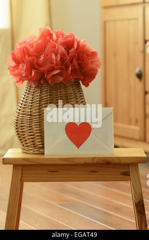 Vaso cesto con red pom pom di carta tissue e fiori Chiusa lettera d'amore su legno piccolo sgabello Foto Stock