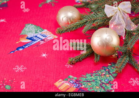 Due golden Natale e un nastro sfere su un abete posto su un rosso tovaglia festiva Foto Stock