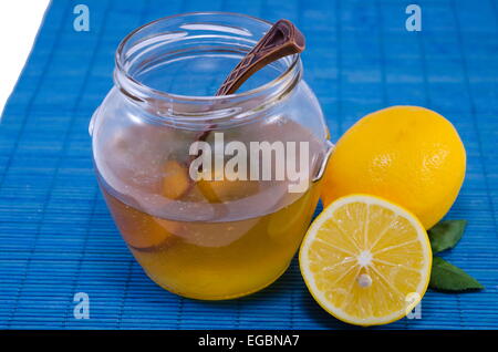 Un vaso di vetro pieno per metà con miele e limoni su sfondo blu con un vintage cucchiaio di legno Foto Stock