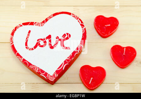 A forma di cuore ad candele rosse e una scatola con la parola "amore ' scritto su di esso, su un sfondo di legno Foto Stock