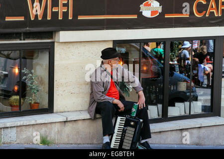 Fisarmonica giocatore seduto sul muro sul lato dell'edificio, Pigalle, Paris, Francia Foto Stock
