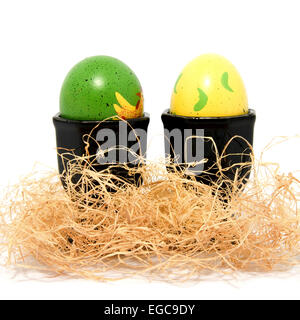 Due dipinti di uova di pasqua in supporti ans la paglia su sfondo bianco Foto Stock