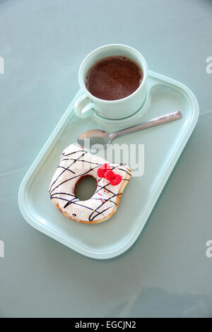 Ciambella e cioccolata calda in un piatto blu sul tavolo da pranzo. Foto Stock