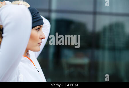 Vista laterale di attraente atleta femminile pronto per una corsa in città. Fiducioso e motivato donna fitness guardando lontano. Foto Stock