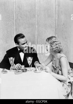 1930s giovane uomo donna abito formale TUXEDO SEDUTA TABELLA CENA ROMANTICA ROMANCE calici di cristallo data Foto Stock