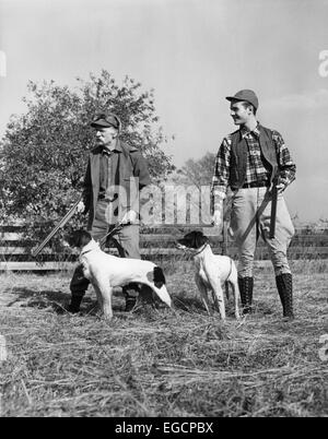 Trenta anni quaranta due uomini giovani e SENIOR ciascuno con un cane da caccia e tiro la pistola IN PIEDI IN UN CAMPO Foto Stock