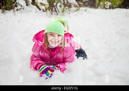 Ridere bambina rendendo volti mentre giocare nella neve nel suo cortile Foto Stock