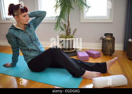 Giovane donna in appoggio su un materassino yoga dopo un allenamento in uno studio con un pianta in vaso su pavimento in legno duro e windows Foto Stock