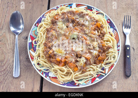 Spaghetti alla bolognese sulla piastra con cucchiaio e forchetta sulla tavola Foto Stock