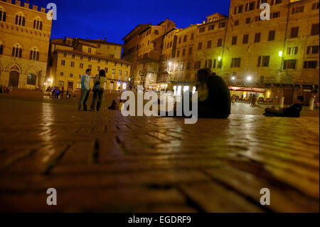 Gli ospiti seduti sulla pavimentazione della piazza del Campo presso il Palazzo Pubblico di Siena, Toscana, Italia Foto Stock