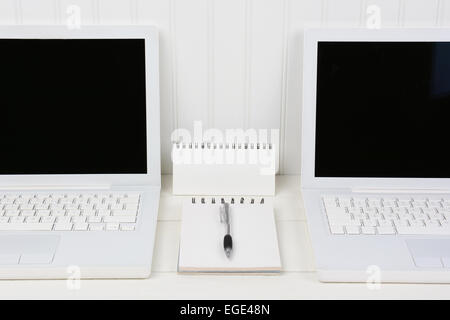 Primo piano dei due notebook in un bianco stazione di lavoro con tampone e penna in mezzo. I calcolatori sono contro una parete beadboard con b Foto Stock