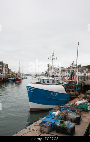 Blu e bianco acciaio commerciale di pesca a strascico legato fino al porto di Weighmouth con granchi e aragoste nasse e reti sul molo Foto Stock