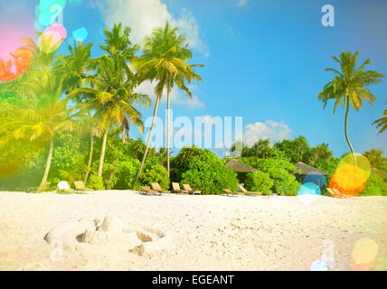 Isola tropicale sulla spiaggia di sabbia con palme e nuvoloso cielo blu. In stile retrò tonica immagine con perdite della luce Foto Stock