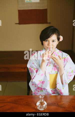 Giovane donna giapponese in uno yukata bere sake Foto Stock