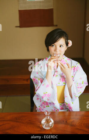 Giovane donna giapponese in uno yukata bere sake Foto Stock