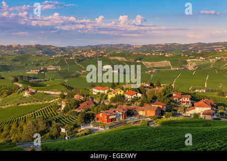 Piccolo villaggio circondato dal verde delle vigne al tramonto in Piemonte, Italia settentrionale. Foto Stock