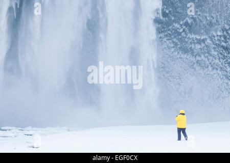 Turista in giacca gialla a cascata Skogafoss in inverno Skogar Sud Islanda Islanda Europa Foto Stock