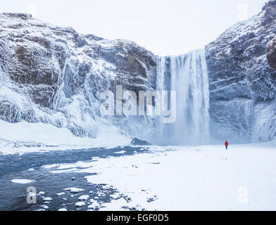 Un Uomo in camicia rossa a cascata Skogafoss in inverno Skogar Sud Islanda Islanda Europa Foto Stock