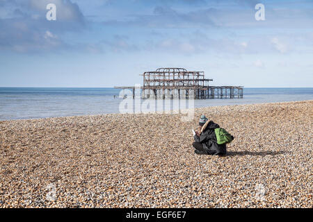 Una donna seduta sulla spiaggia di Brighton. Foto Stock