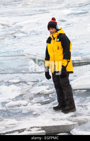 Tourist standing su ghiaccio alla Laguna Glaciale di Jokulsarlon, sul bordo del Parco Nazionale di Vatnajokull, Islanda nel mese di febbraio Foto Stock