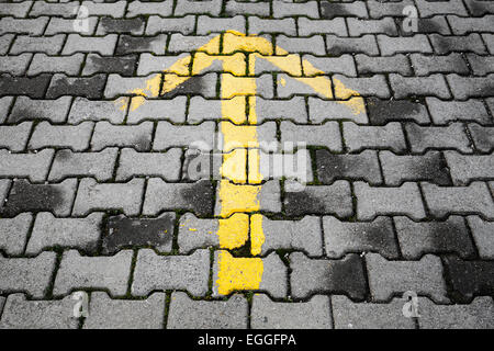 Una freccia gialla dipinta sul grigio scuro cobblestone pavement, direzione strada segno Foto Stock