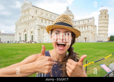 Ritratto di felice giovane donna che mostra i pollici fino a piazza dei Miracoli a Pisa, Toscana, Italia Foto Stock