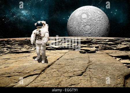 Un astronauta sondaggi la sua situazione dopo essere stata fregata su un pianeta sterile. Un grande, pesantemente ingabbiati luna sorge all'orizzonte. Foto Stock