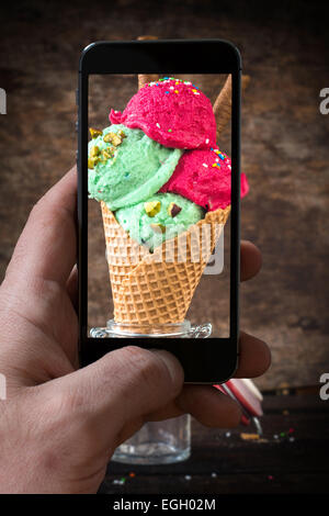 Gelato con pistacchi e fragola nel cono di fotografare dalla fotocamera del telefono Foto Stock