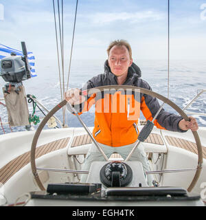 Giovane Skipper di mattina presto al timone di una barca in mare aperto. Foto Stock