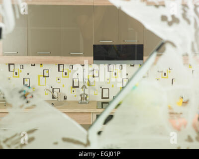 Lavaggio del cristallo con spatola e detergente, con cucina domestica in background Foto Stock