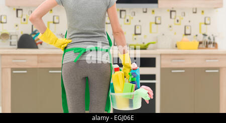 Vista posteriore della donna delle pulizie in piedi in cucina tenendo la benna con prodotti per la pulizia Foto Stock
