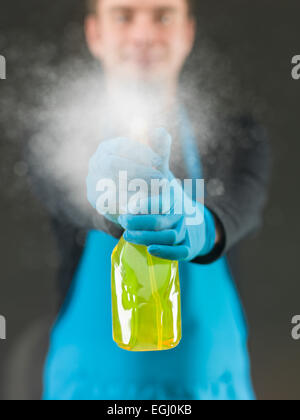 Lavoratore di pulizia la spruzzatura di liquido detergente sulla superficie della finestra davanti a lui Foto Stock